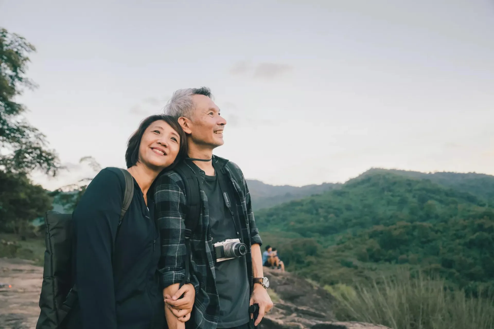 Asian couple hiking on top of a mountain enjoying sunset over the tropical valley.